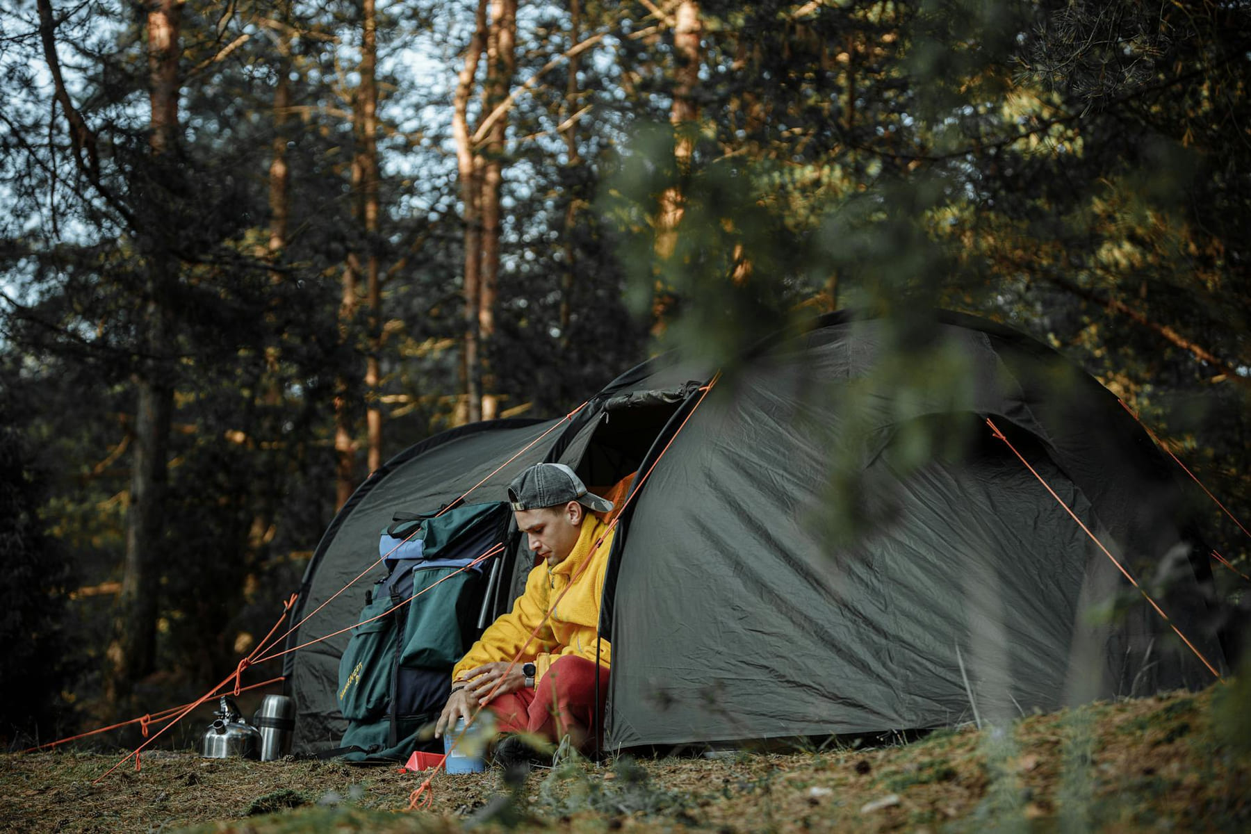 A man sitting by his tent in a forested campsite during the day. on The Frugal Camper
