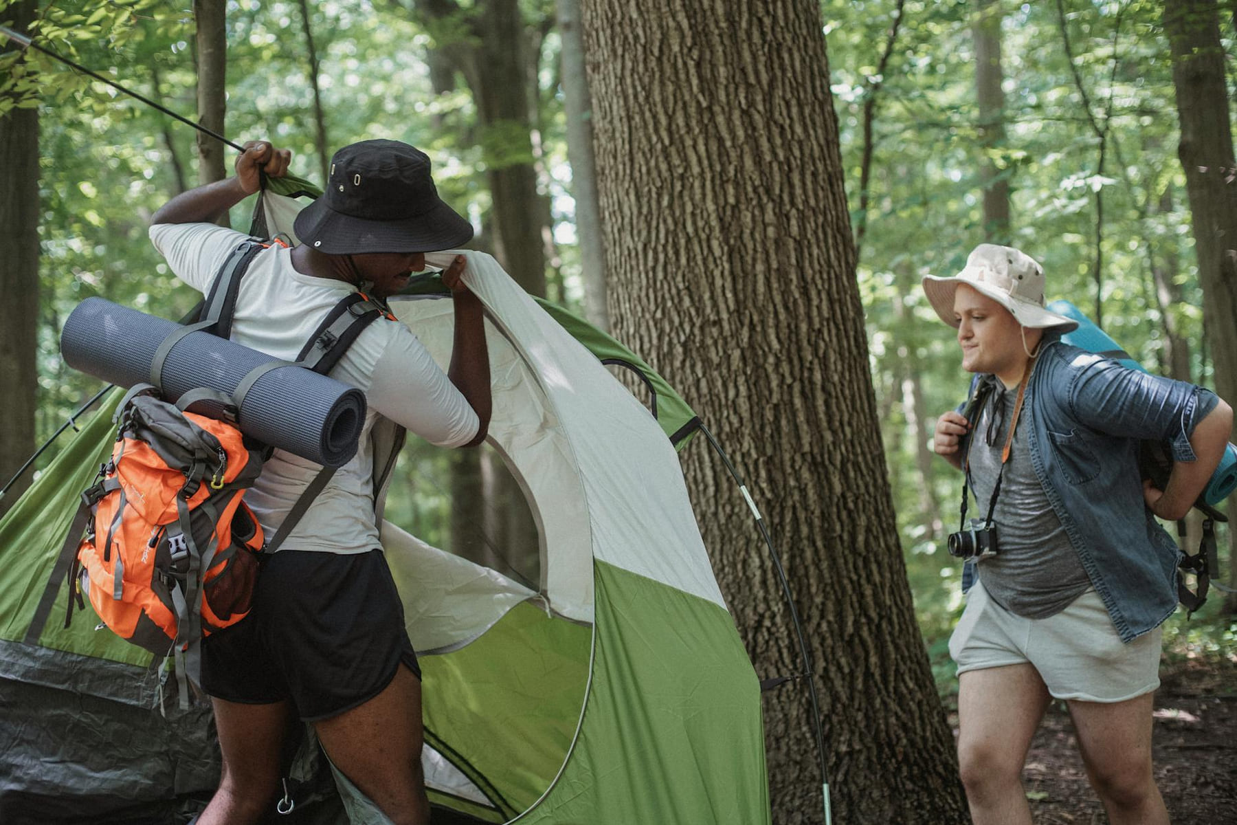 Concentrated young multiracial male hikers in casual clothes and hats with backpacks setting up tent in forest while preparing for recreation during trip on The Frugal Camper