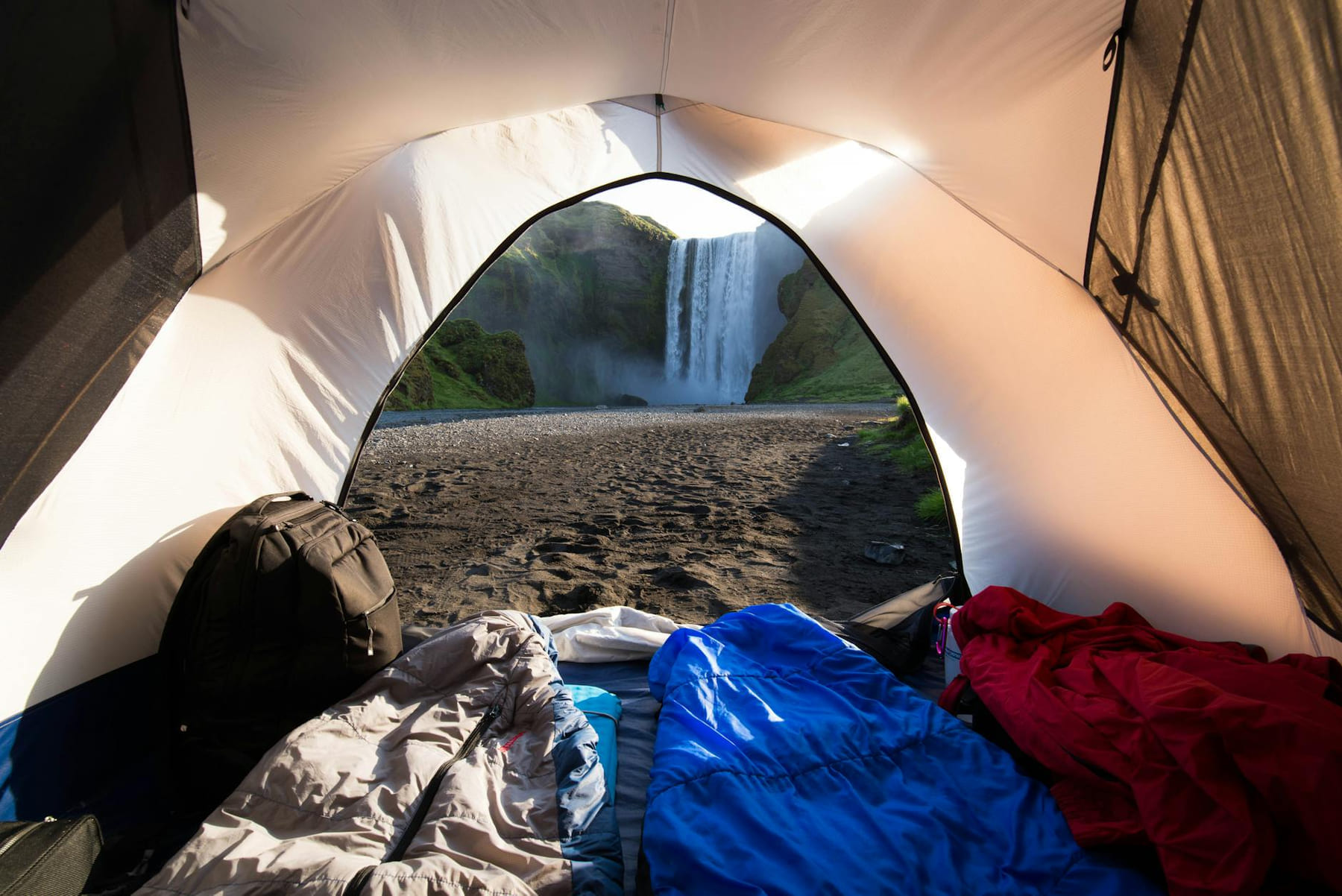 View from a camping tent interior looking at a scenic waterfall in a wilderness setting. on The Frugal Camper