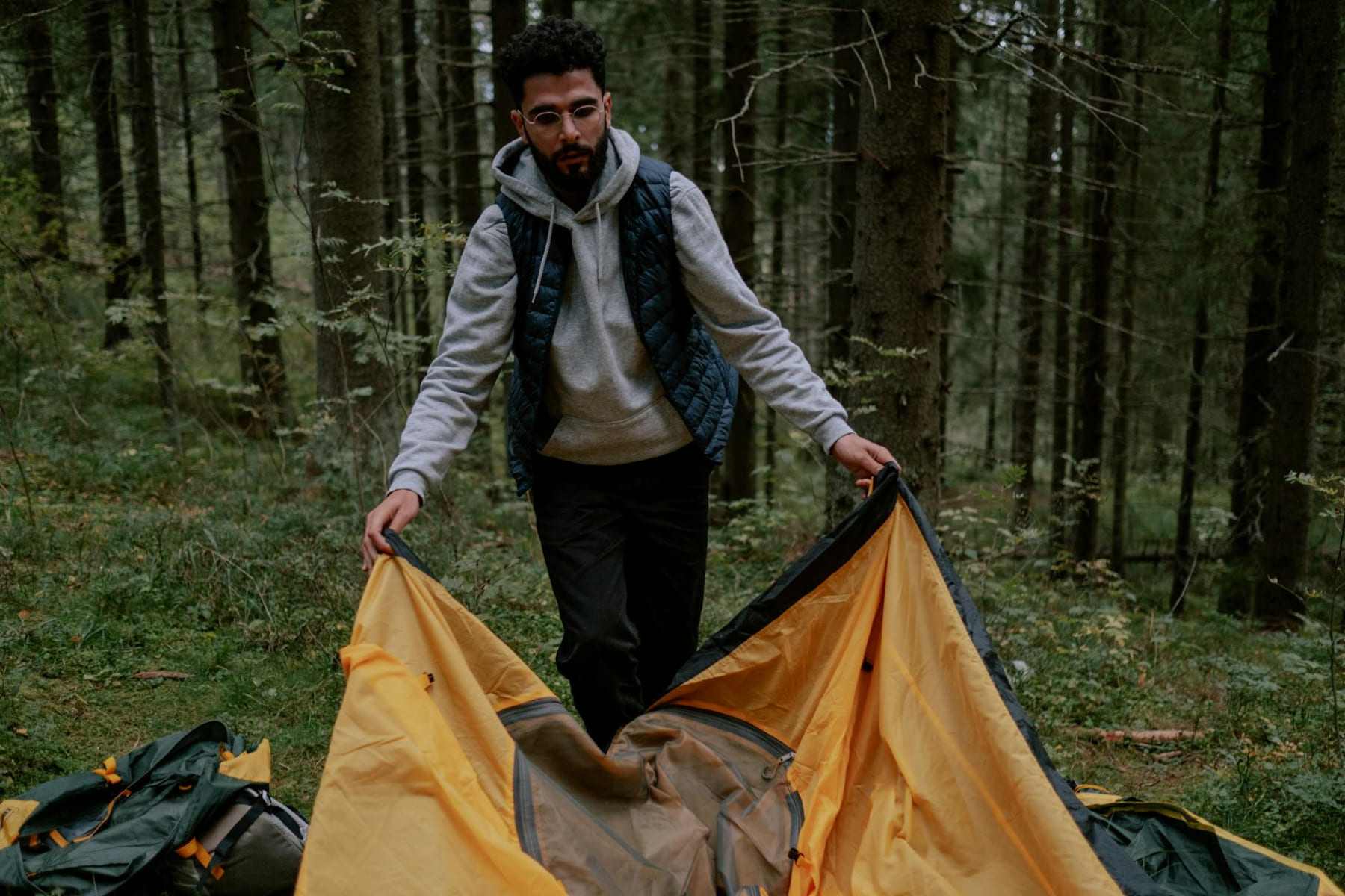 Man setting up a yellow tent in the forest, preparing for camping adventure. on The Frugal Camper