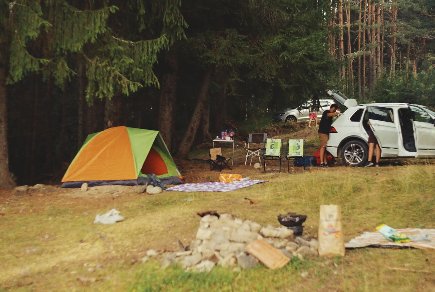 Explore a peaceful camping scene in the forest with a tent, car, and campfire setup. on The Frugal Camper
