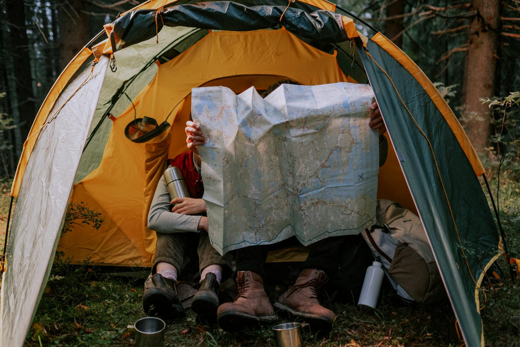 Two people enjoy a camping trip, examining a map inside a tent surrounded by nature. on The Frugal Camper