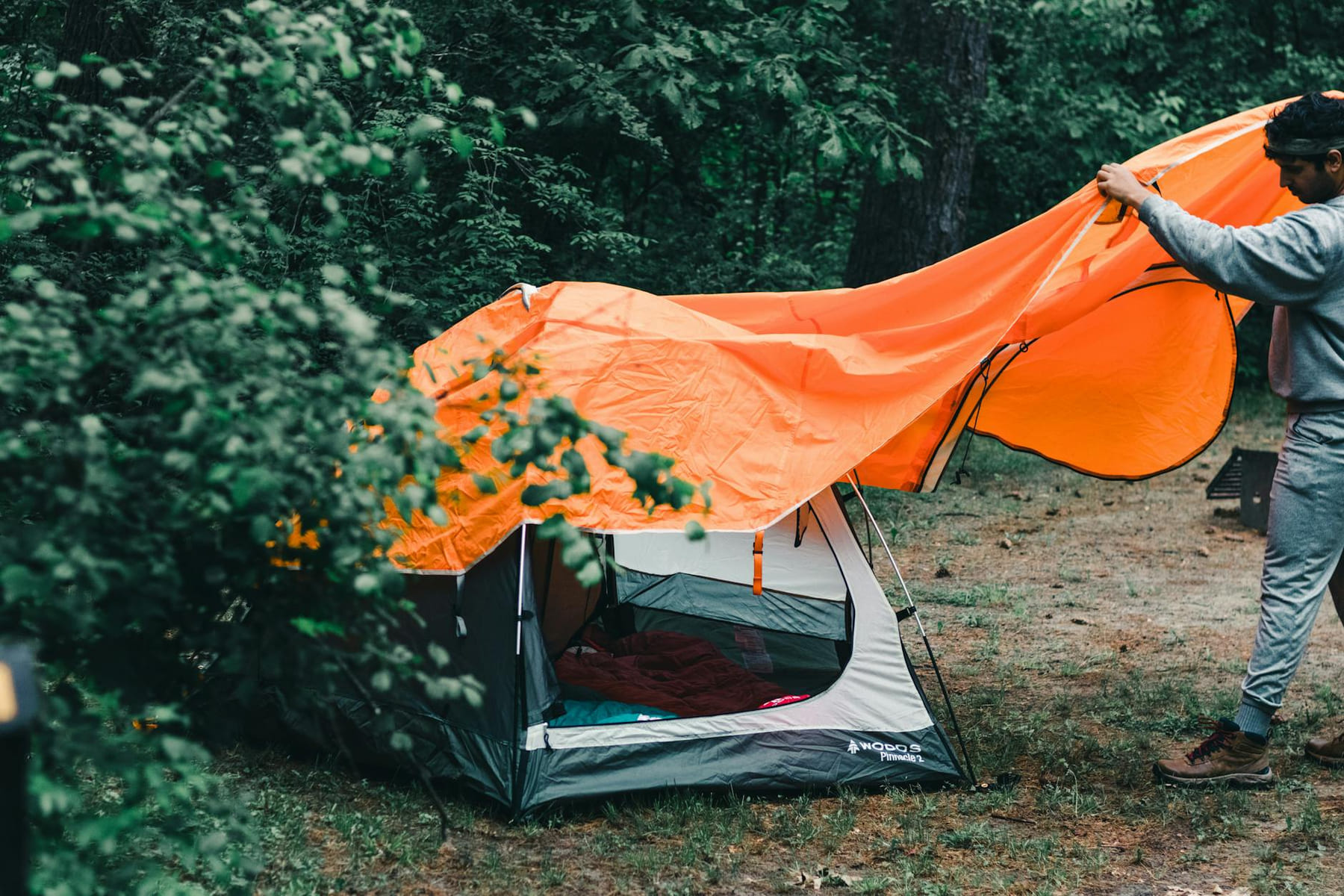 A man sets up a tent in a lush Canadian forest, perfect for summer camping adventures. on The Frugal Camper