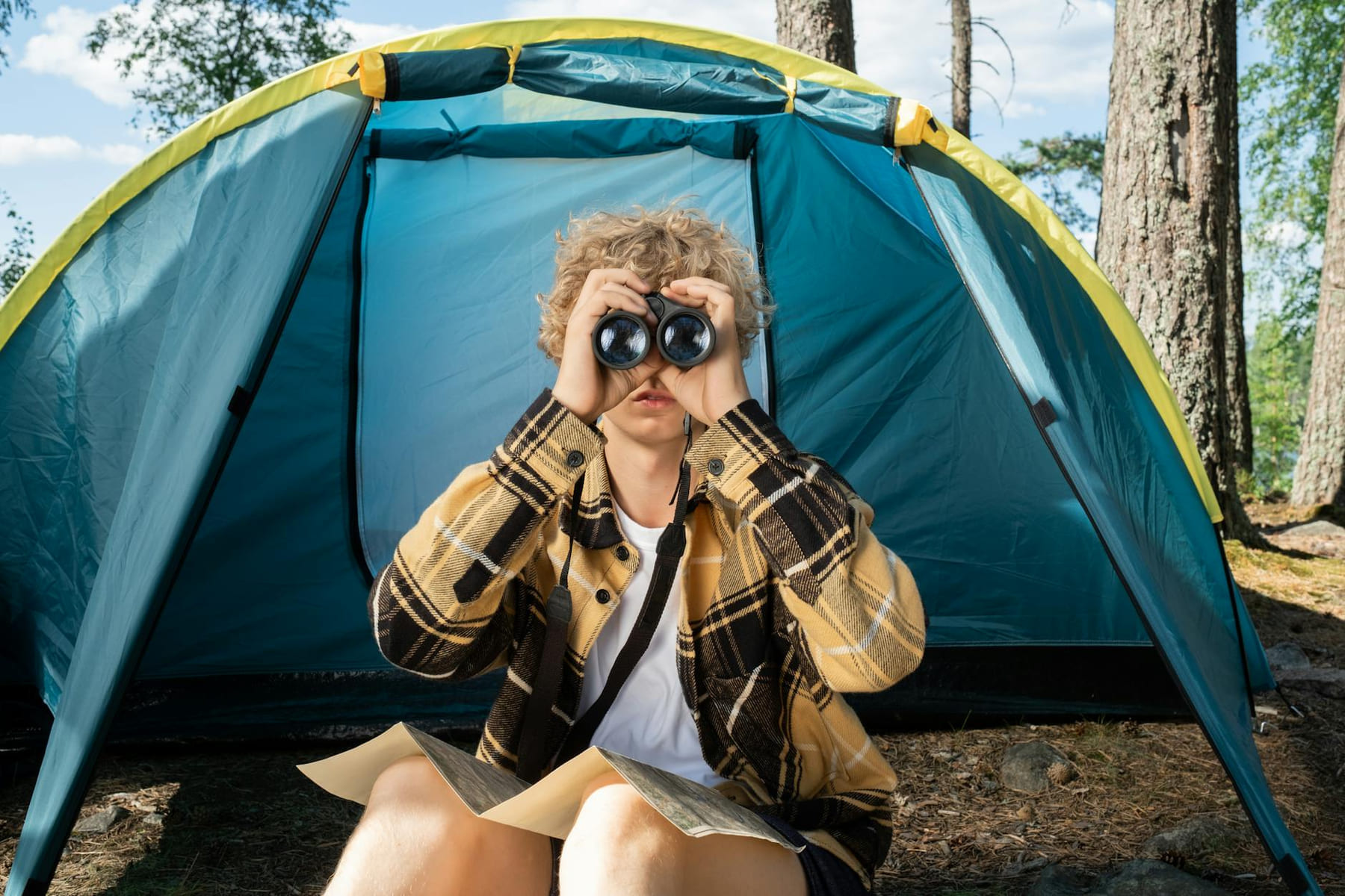 Teen camping with binoculars and a map, exploring the outdoors in summer. on The Frugal Camper