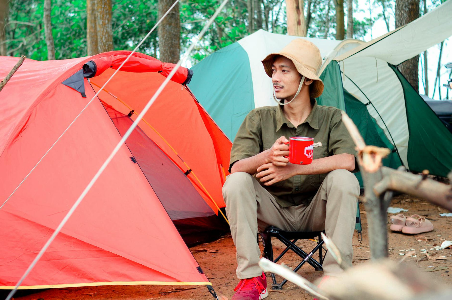 Man sitting outdoors with a red cup near tents in the forest, enjoying camping. on The Frugal Camper