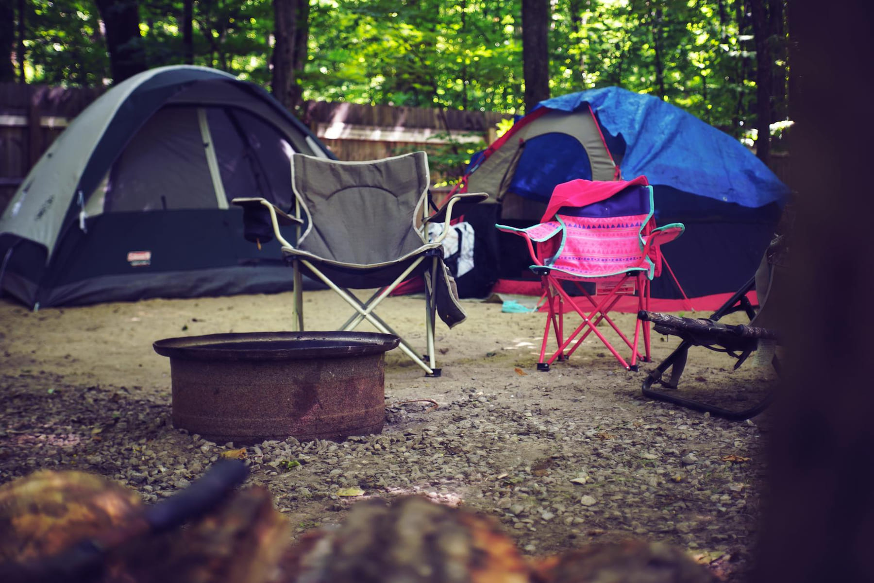 A serene campsite in the woods with colorful tents, camping chairs, and a fire pit, perfect for a leisure getaway. on The Frugal Camper