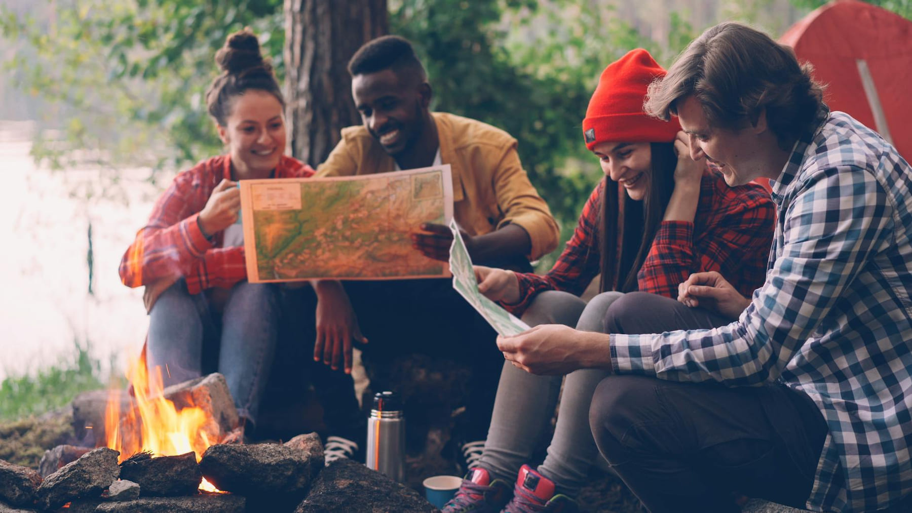 Group of friends enjoying a camping trip, reading a map by the campfire. on The Frugal Camper
