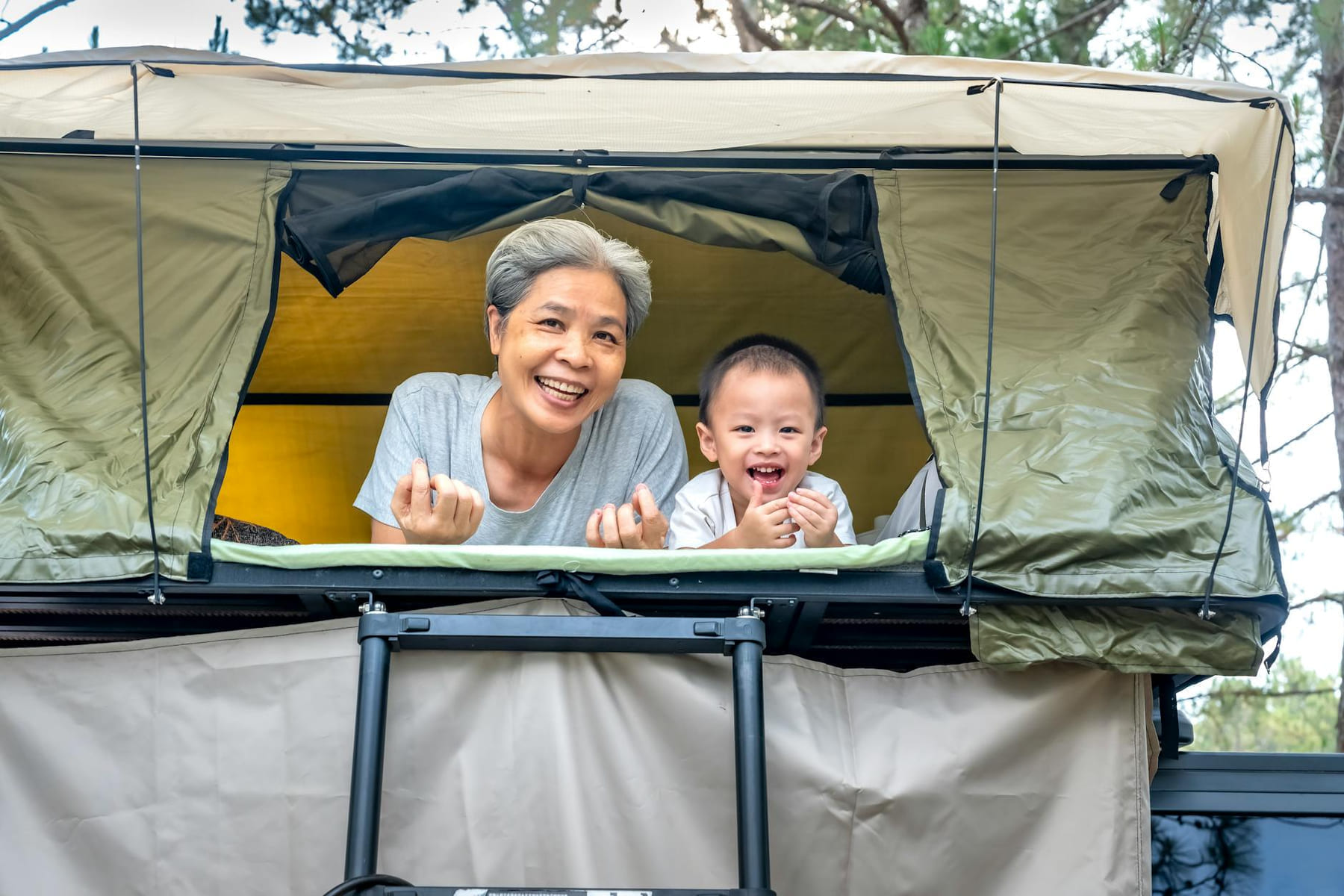 Smiling grandmother with child in a rooftop tent during a joyful camping trip. on The Frugal Camper