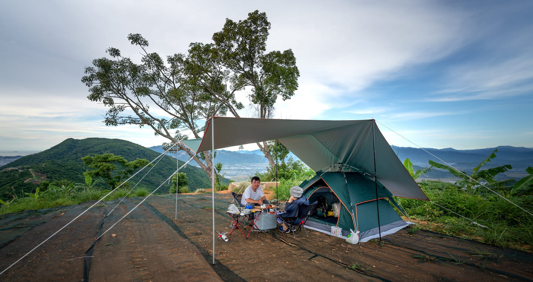 Outdoor camping scene with tent and tarp in a mountainous area during daytime. on The Frugal Camper